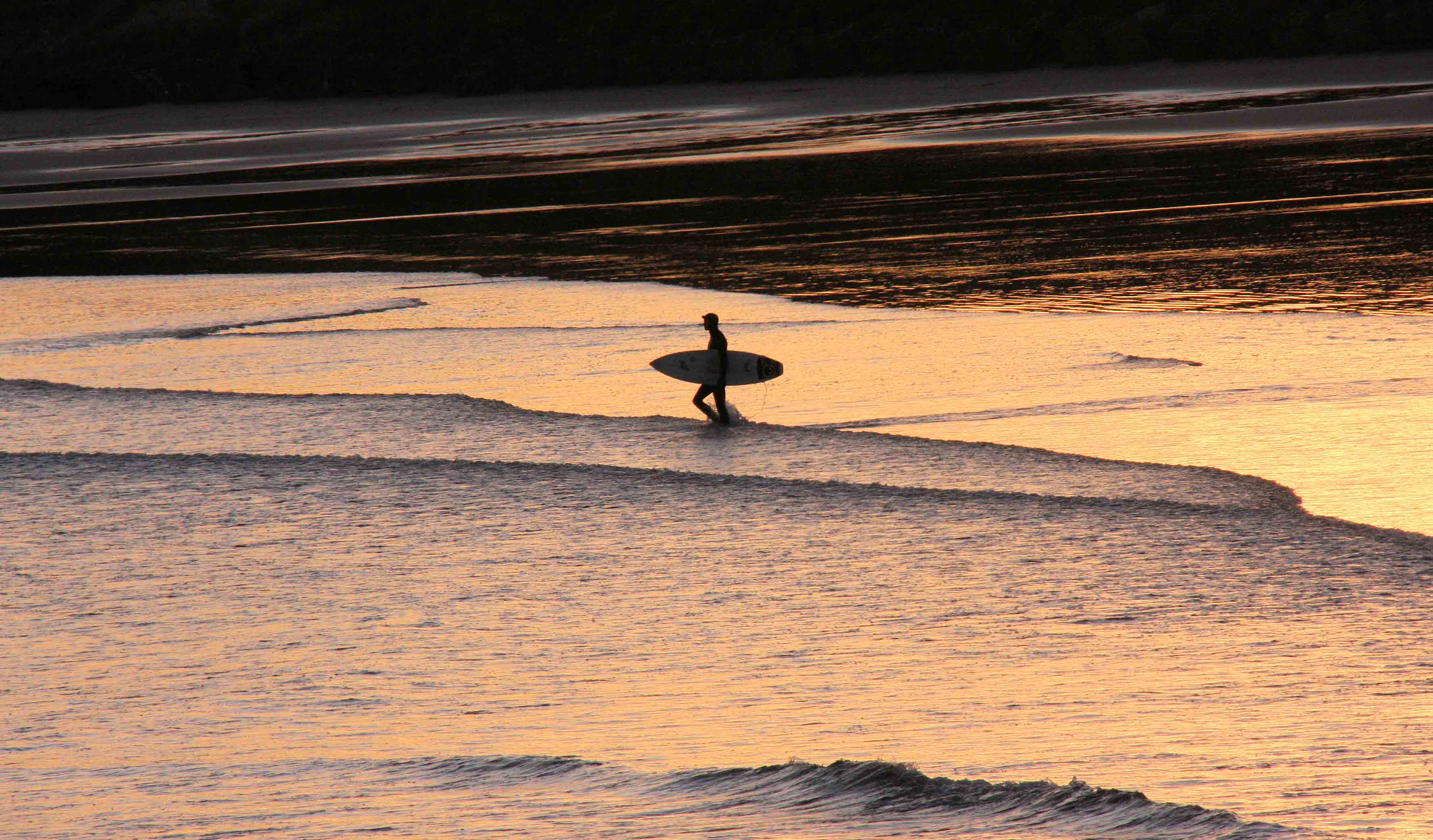 En mann med surfebrett går gjennom bølgene på en strand.