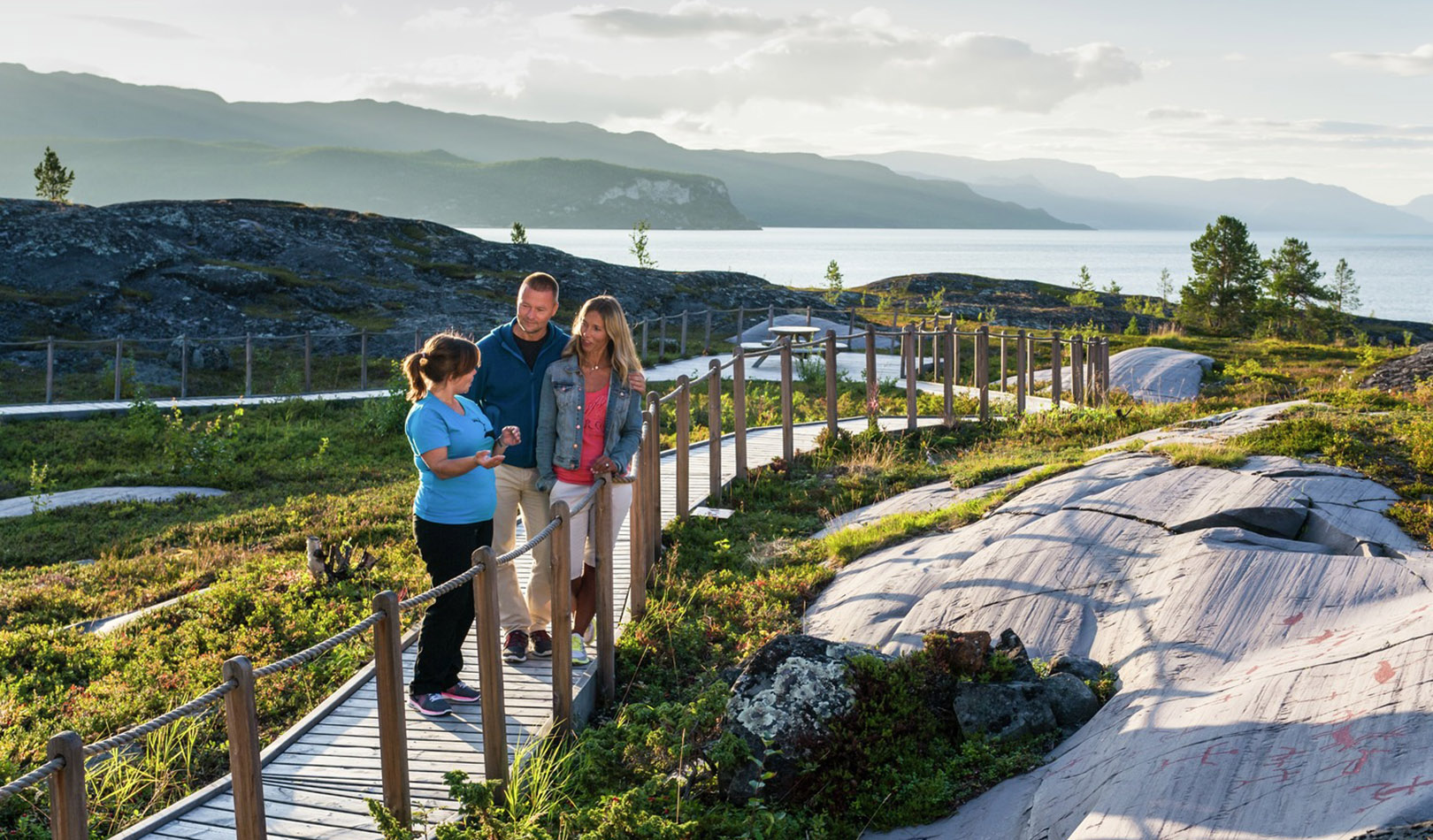 Turister ser på helleristninger i Alta med flott natur rundt. T