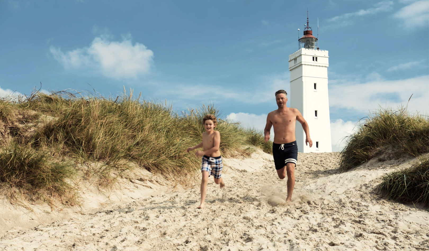 Father and son running on the beach with a lighthouse in the background 