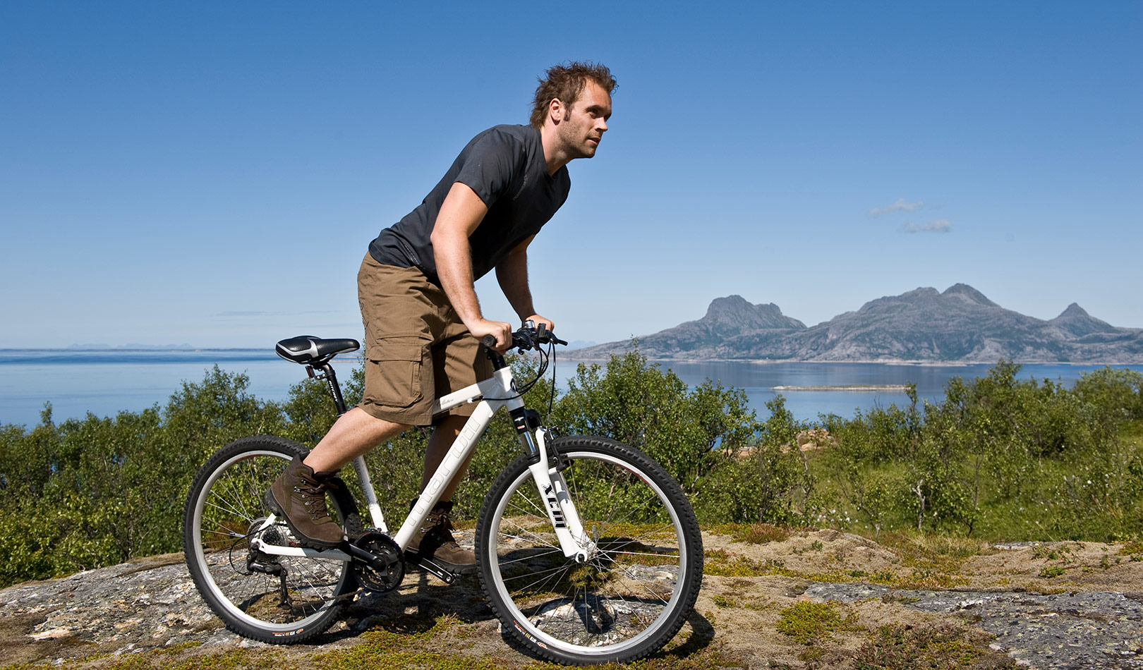 A man biking up the mountain Keiservarden i Bodø with the island Landegode in the background.