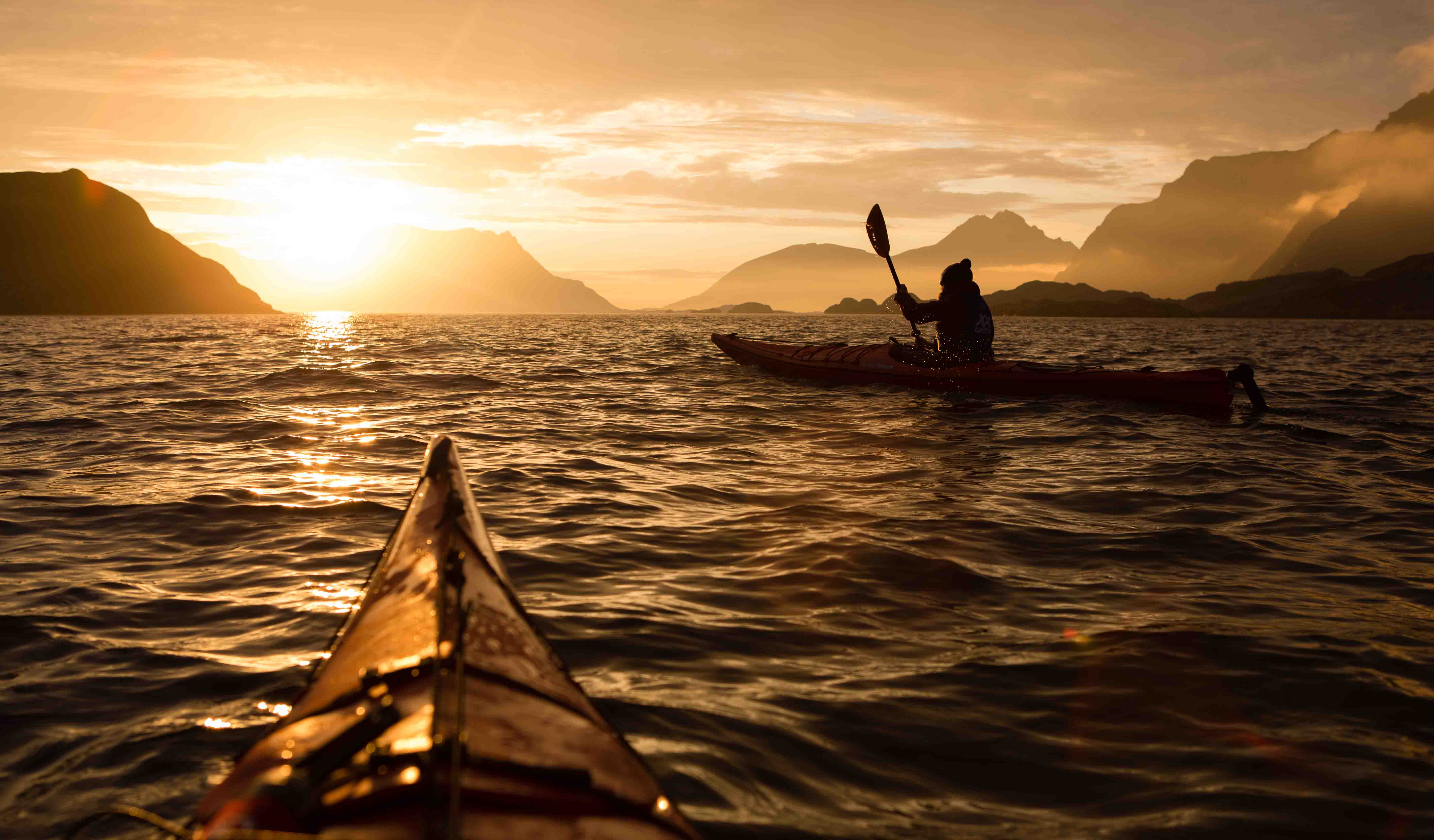 To kajakker under midnattsola ved kysten av Vestvågøy, Lofoten. Two kayakers below the midnight sun on the coastline of Vestvågøy, Lofoten.
