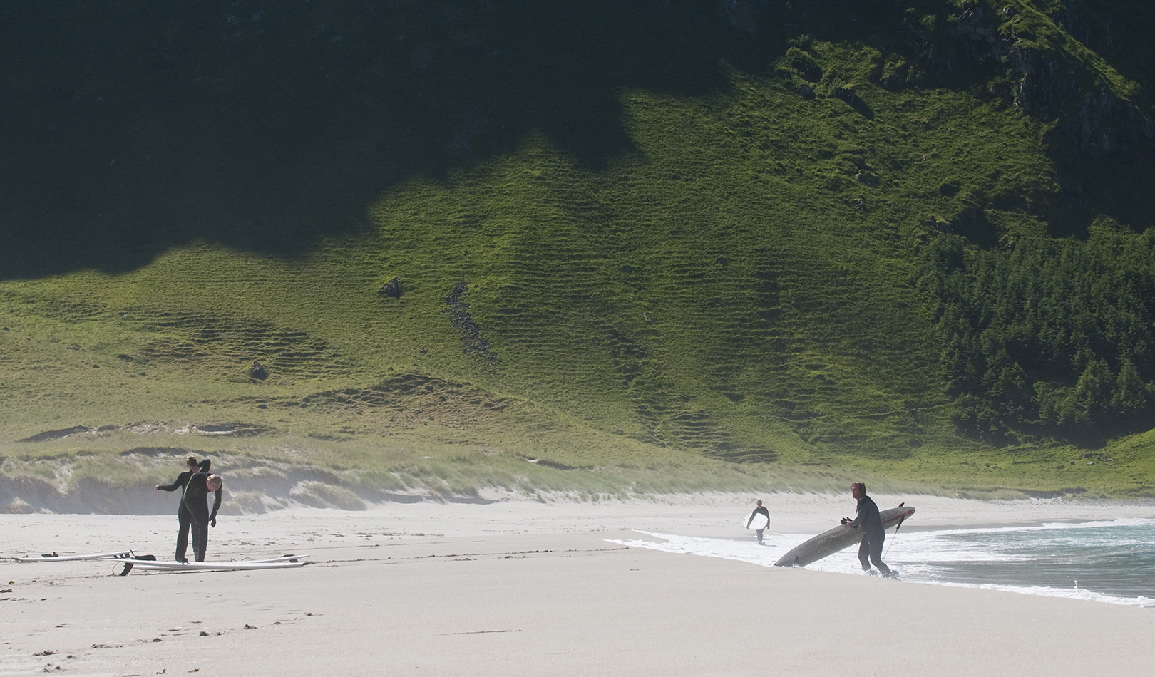 Surfere på Hoddevik strand med sand og grønn fjellside. 