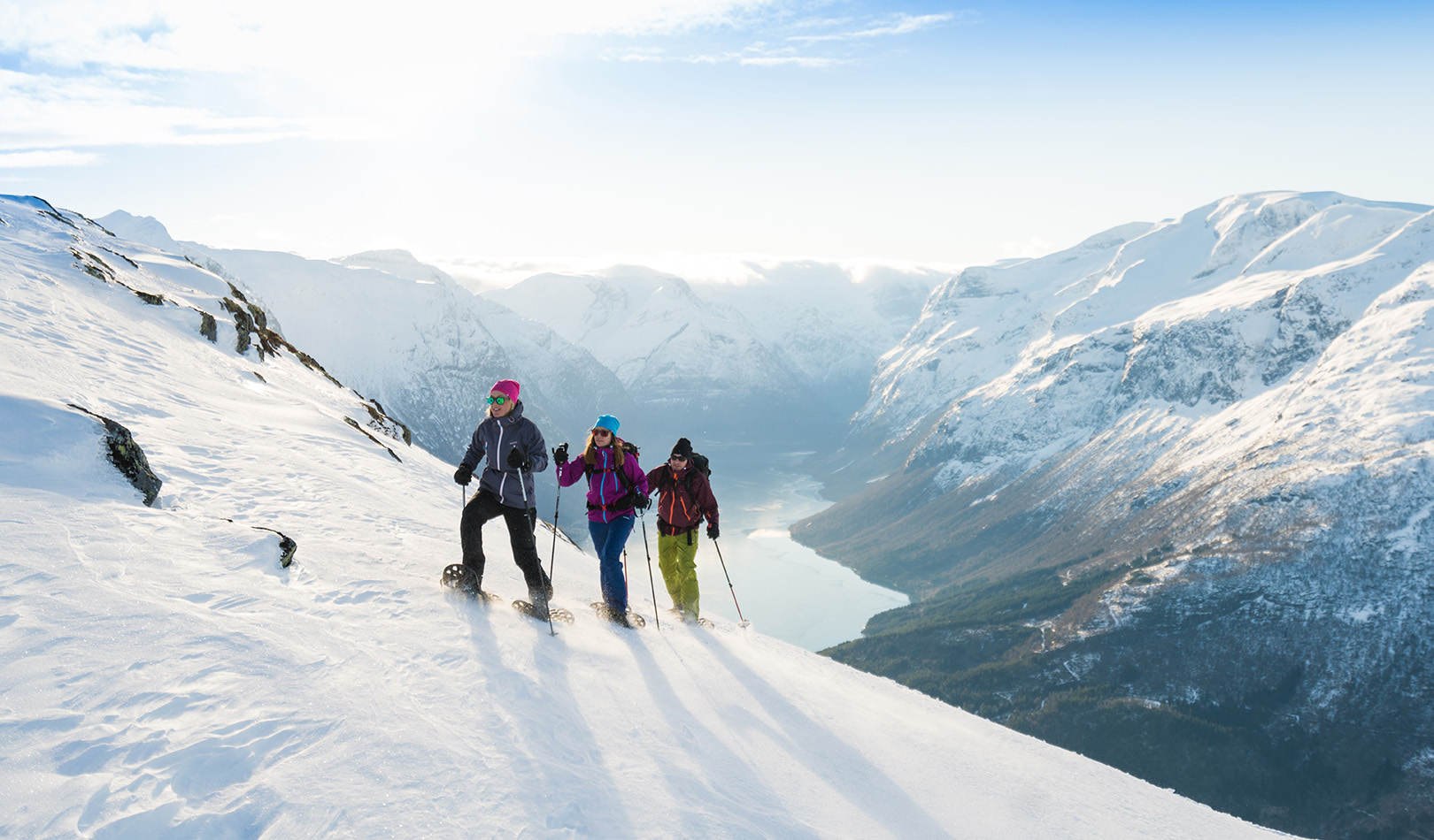 Tre personer går på truger på fjellet Hoven i Loen, Stryn med fantastiske vinterfjell i bakgrunnen. 