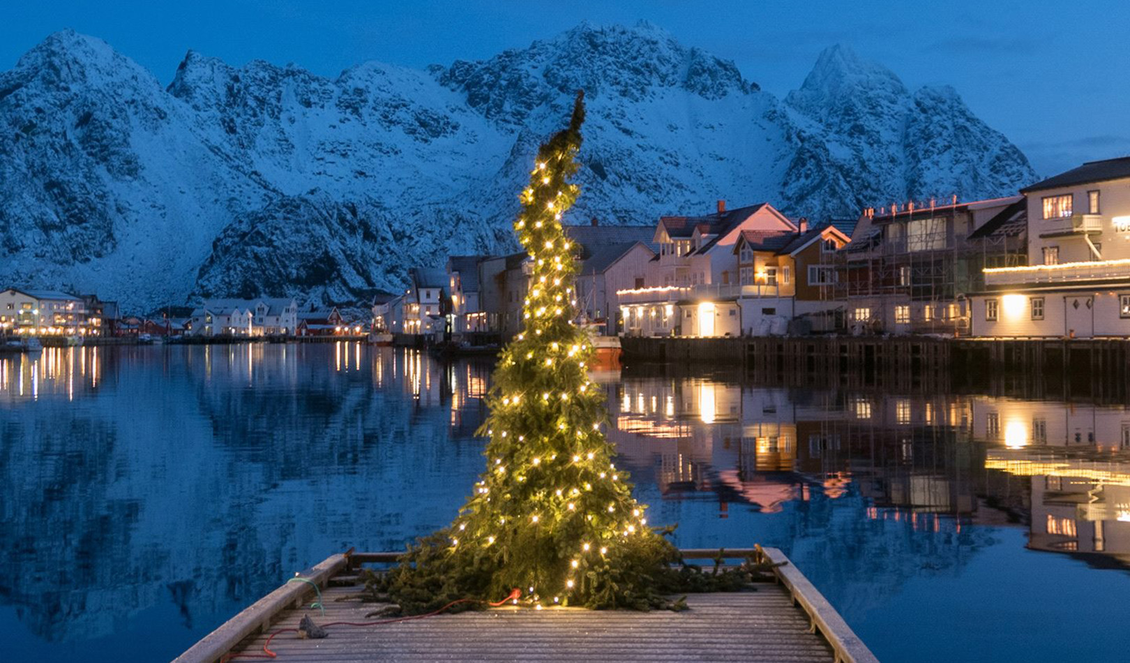 Juletre på brygga med hus og fjell i Henningsvær i bakgrunnen.