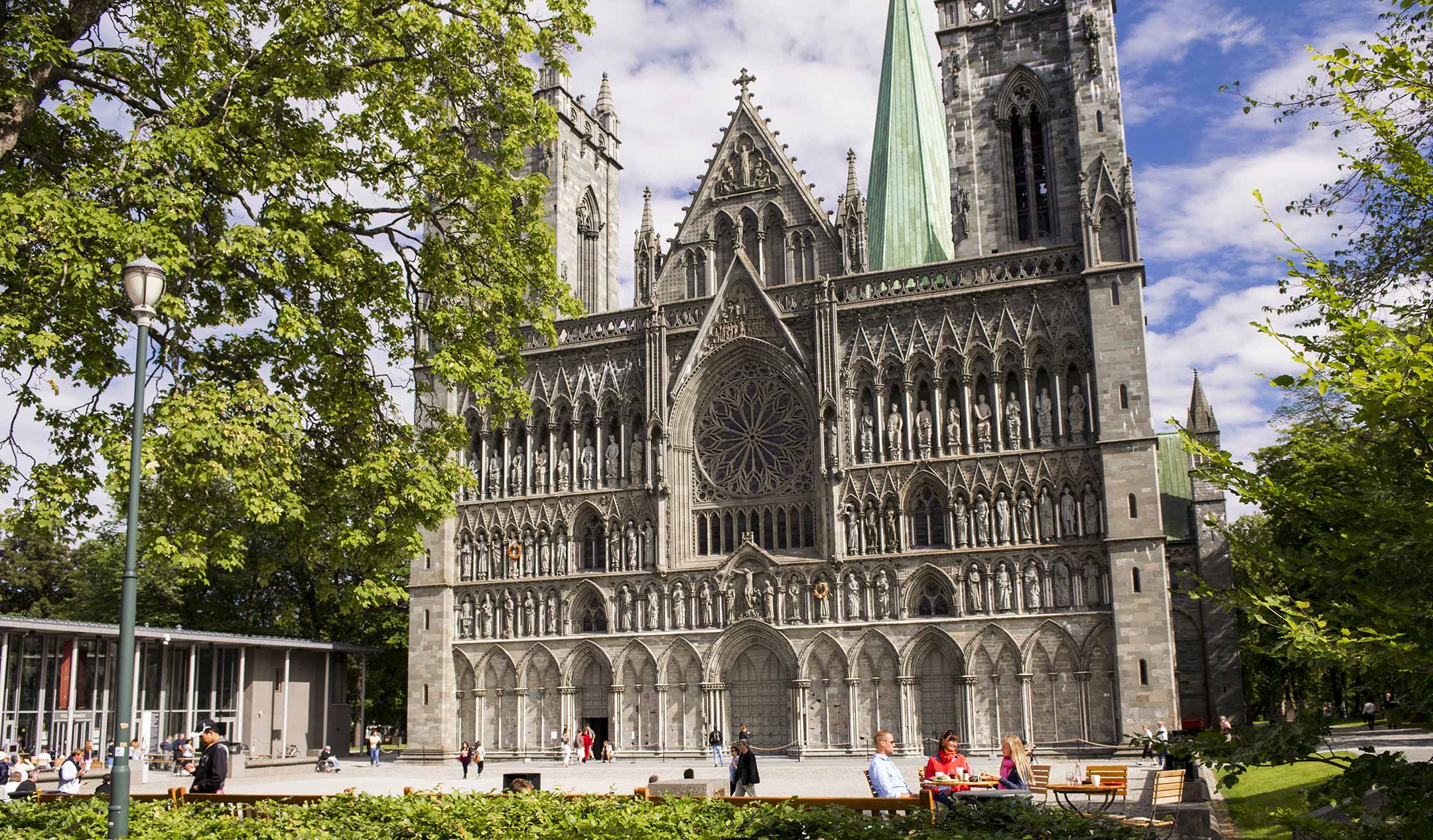 Nidarosdomen in Trondheim in the sunlight, with trees in the background and people in the foreground