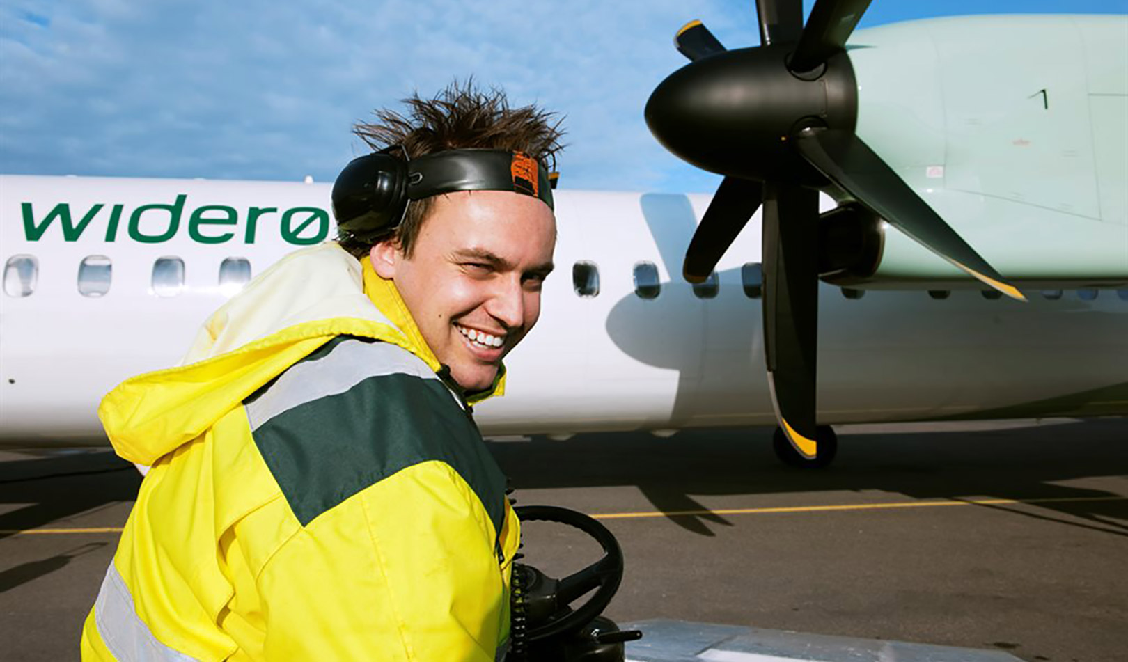 Smilende flyplassansatt ved et Widerøefly på Torp flyplass, Sandefjord.