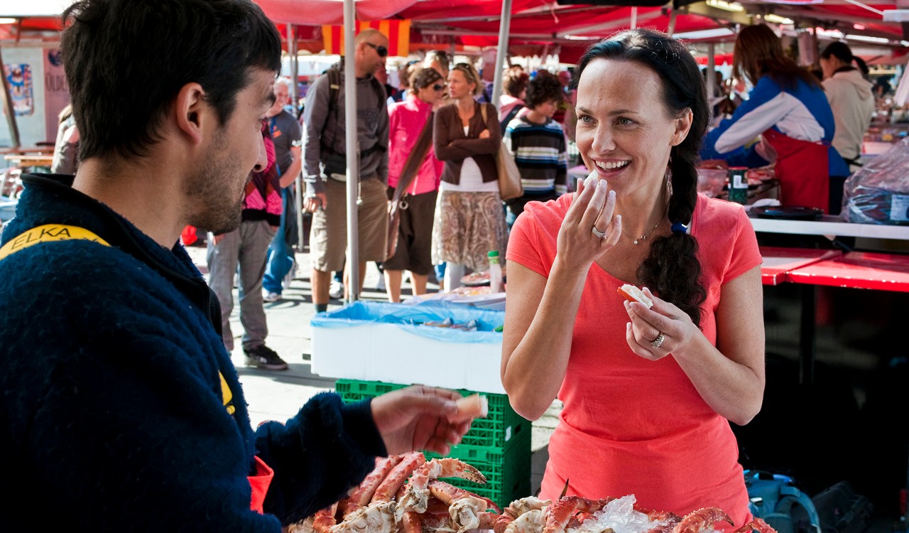 Dame får smaksprøve av selger på Fisketorget i Bergen. Woman gets a sample from a seller at the market place in Bergen.