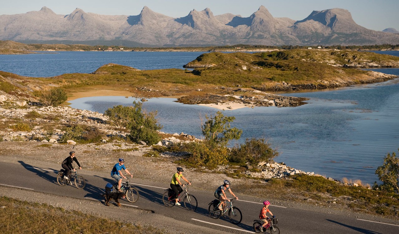 Syklister på Herøy med fjellrekken De syv søstre i bakgrunnen i Helgeland i Nordland. Cyclists in Herøy with the mountainrange The seven sisters in the Background in Helgeland, Nordland.