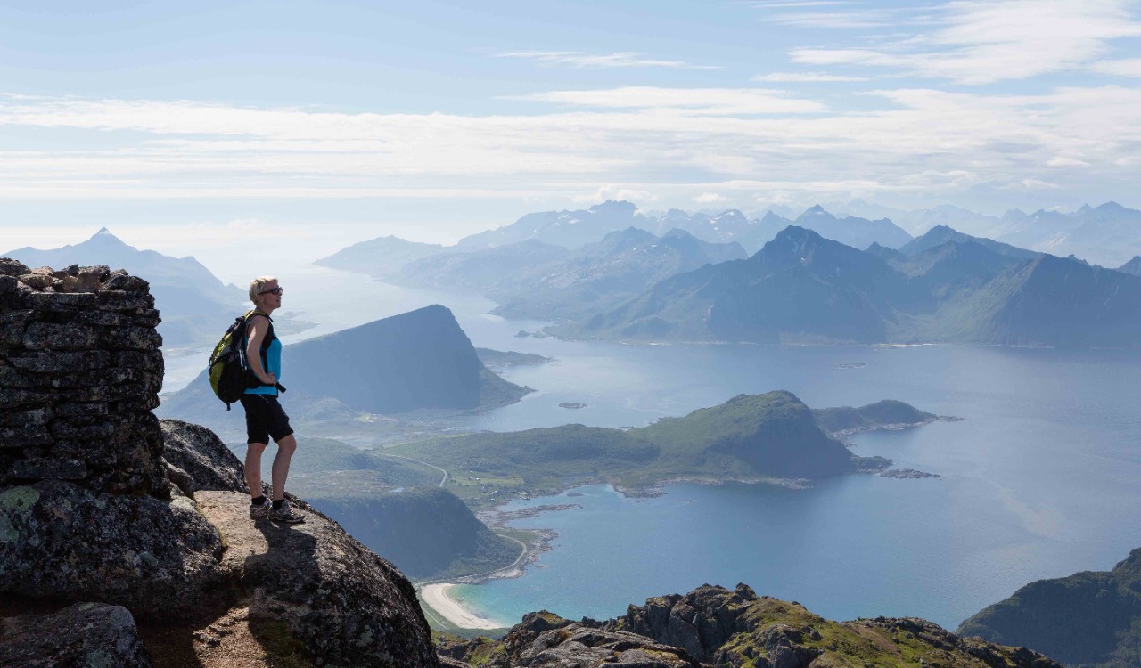 Kvinnelig turgåer ser utover fjell og hav på Flakstad, Lofoten. Woman enjoying the view from a mountain top in Flakstad, Lofoten.