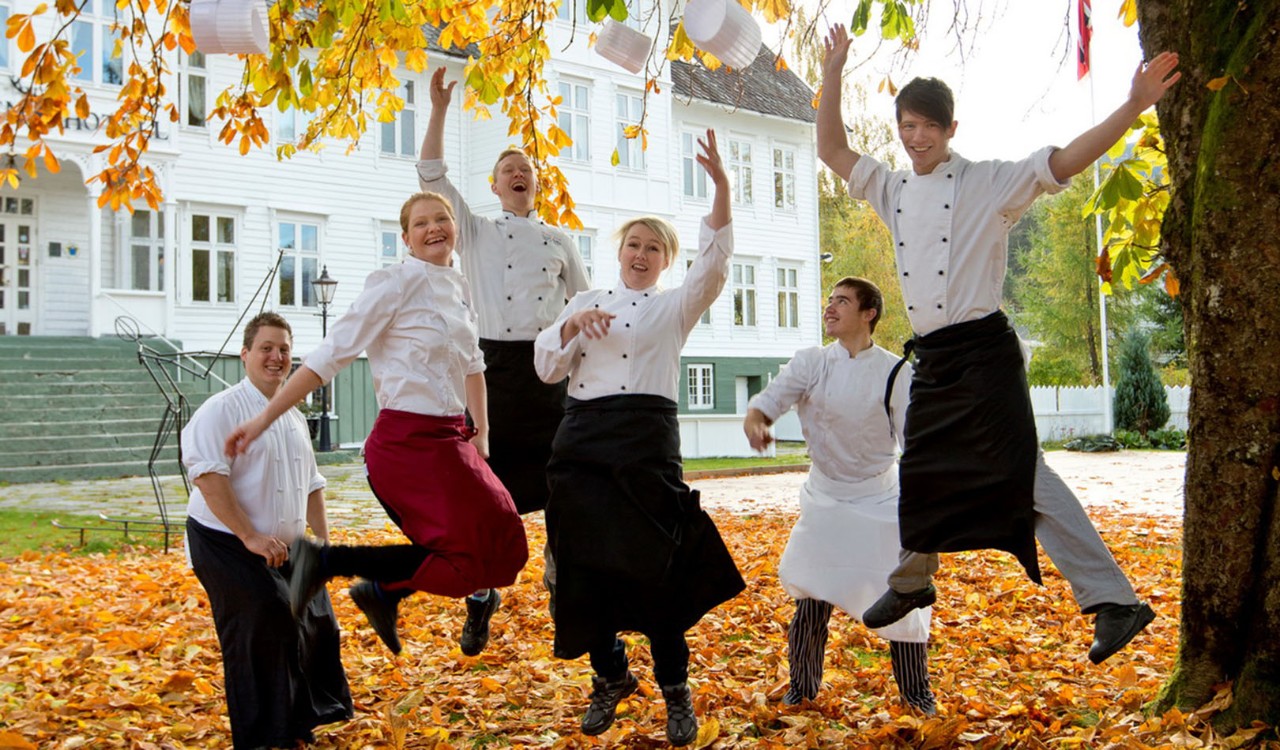 Hoppende kokker i høstløvet utenfor Gloppen Hotell. Jumping chefs outside Gloppen Hotel surrounded by autumn leaves.