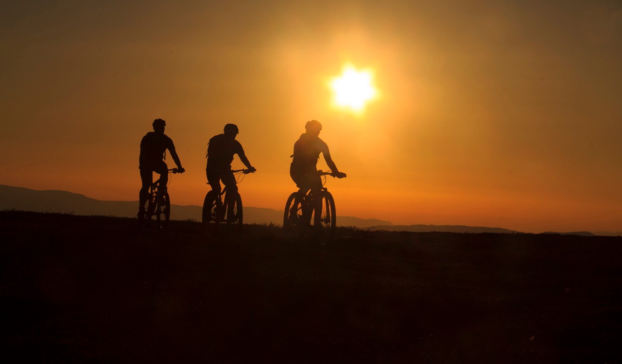 Silhuett av tre syklister på Finnmarksvidda i glødende midnattsol. Silhouette of three cyclists on the Finnmark plateau in glowing midnight  sun.