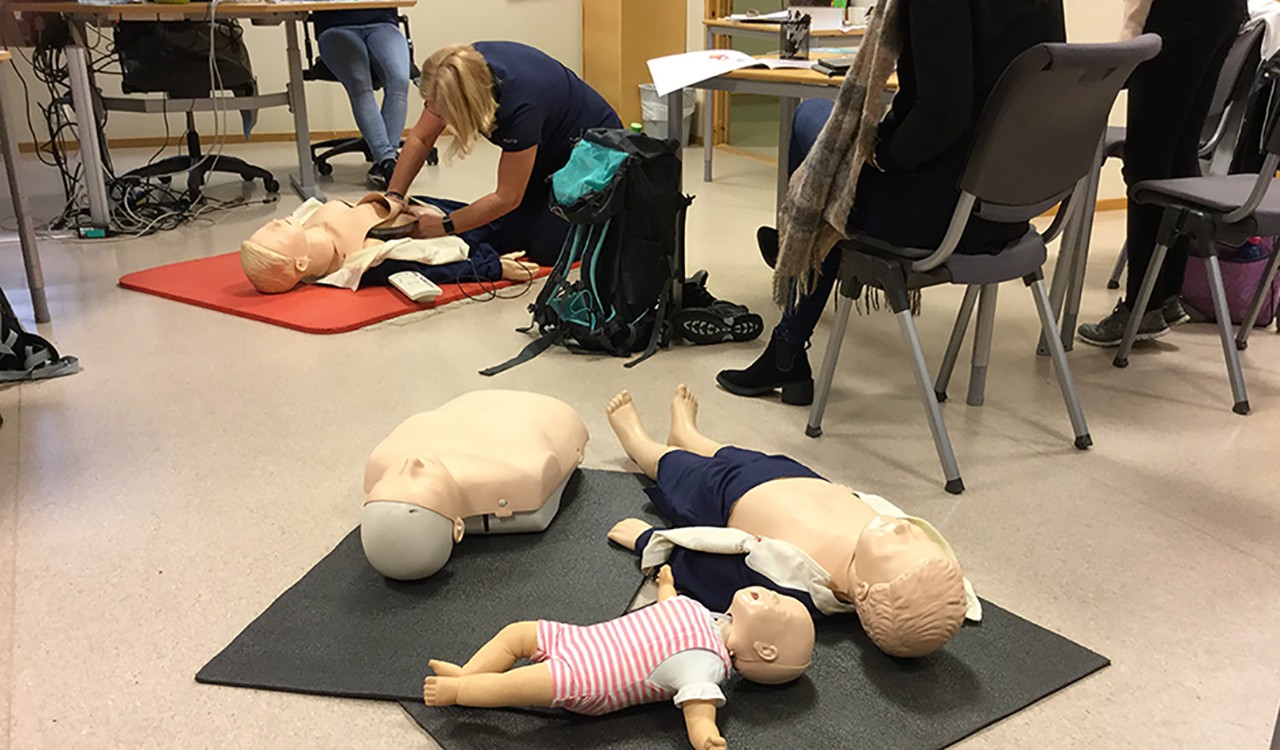Deltakere på et kabinkurs hvor en kvinne demonstrerer hjerte-lunge redning på en dukke. Participants in a Widerøe cabin course demonstrating cardiac resuscitation.