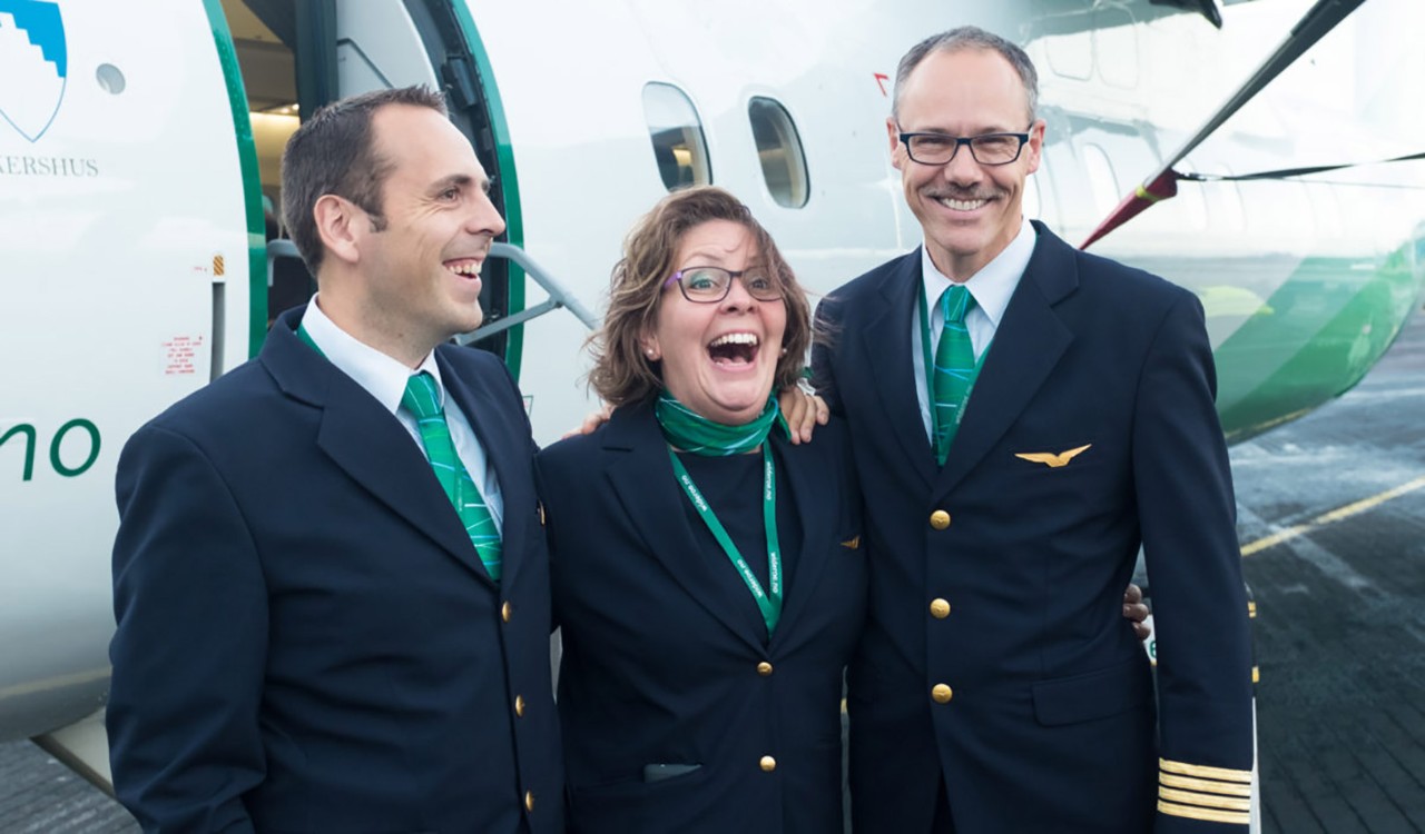 Tre glade Widerøe-ansatte foran et fly. Three happy Widerøe employees in front of an aircraft.