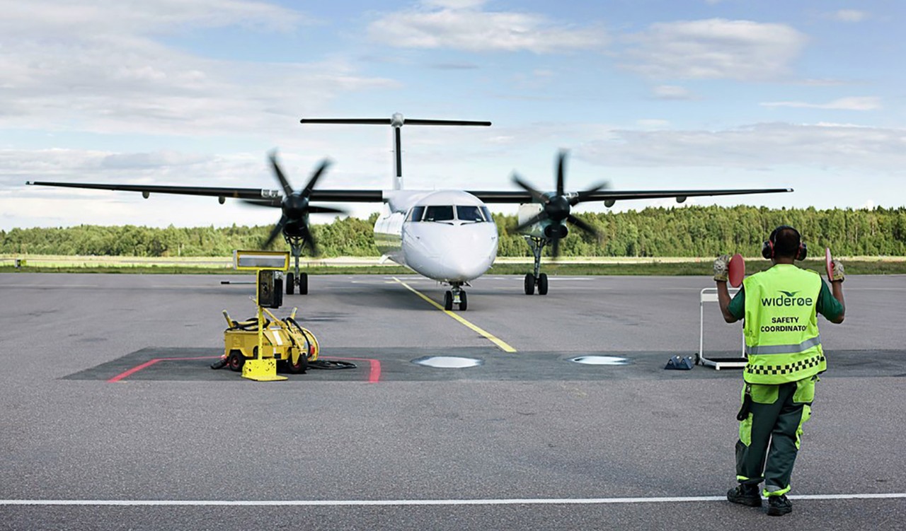 Widerøe-fly og flyplassansatt på en flyplass. Widerøe plane and airport employee on the airport.