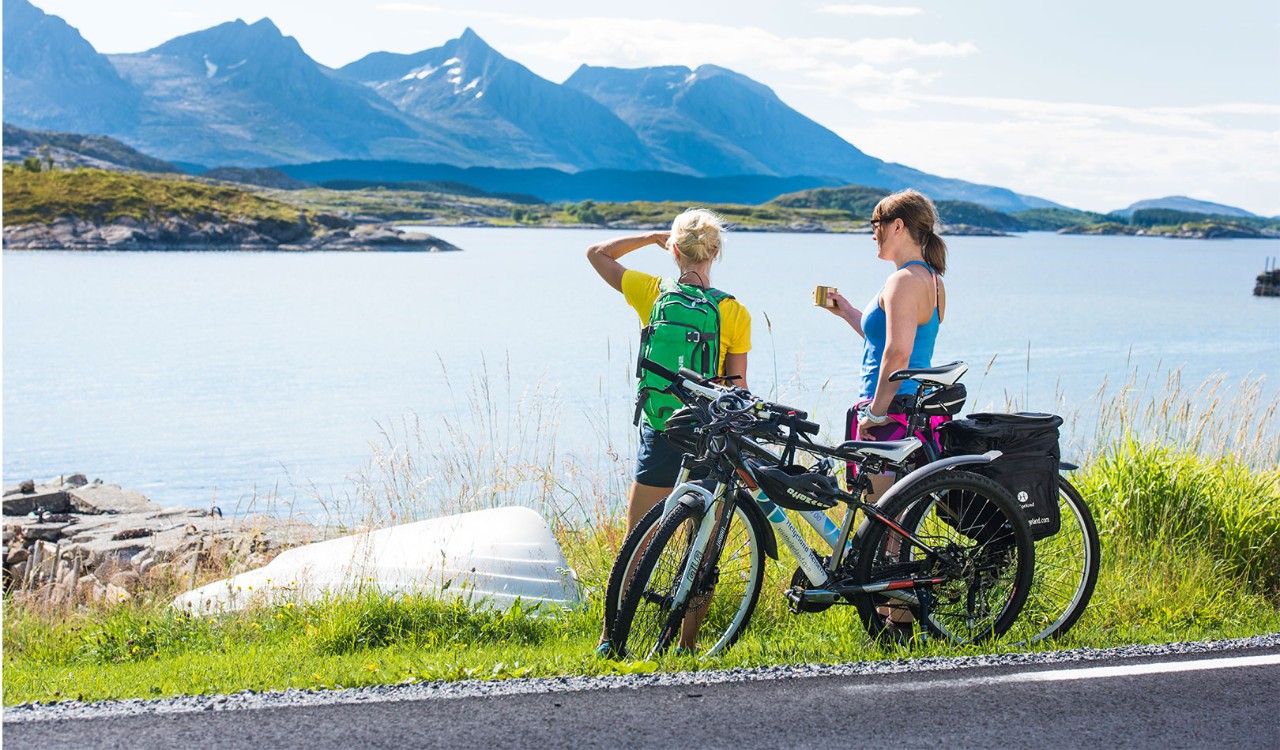 Par nyter sol og hav fra bryggekant med sykler i Helgeland. Couple with bikes enjoying the view over ocean and sun in Helgeland.