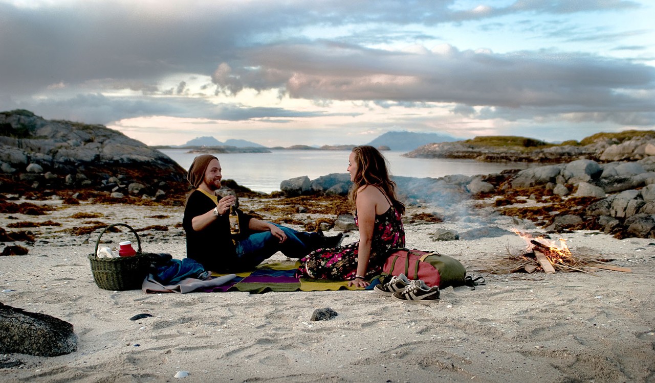 Ungt par har piknik med bål på stranda, Helgeland. Young couple having a picnic on the beach with bonfire.