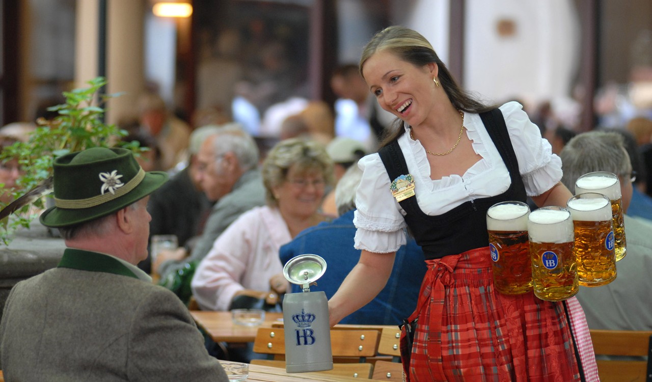 En kvinne I tradisjonelt bayersk kostyme serverer øl til en mann på tavernaen Hofbräuhaus i München. A woman in a traditional Bayern costume serving beer to a man at the Hofbräuhaus in Munich.