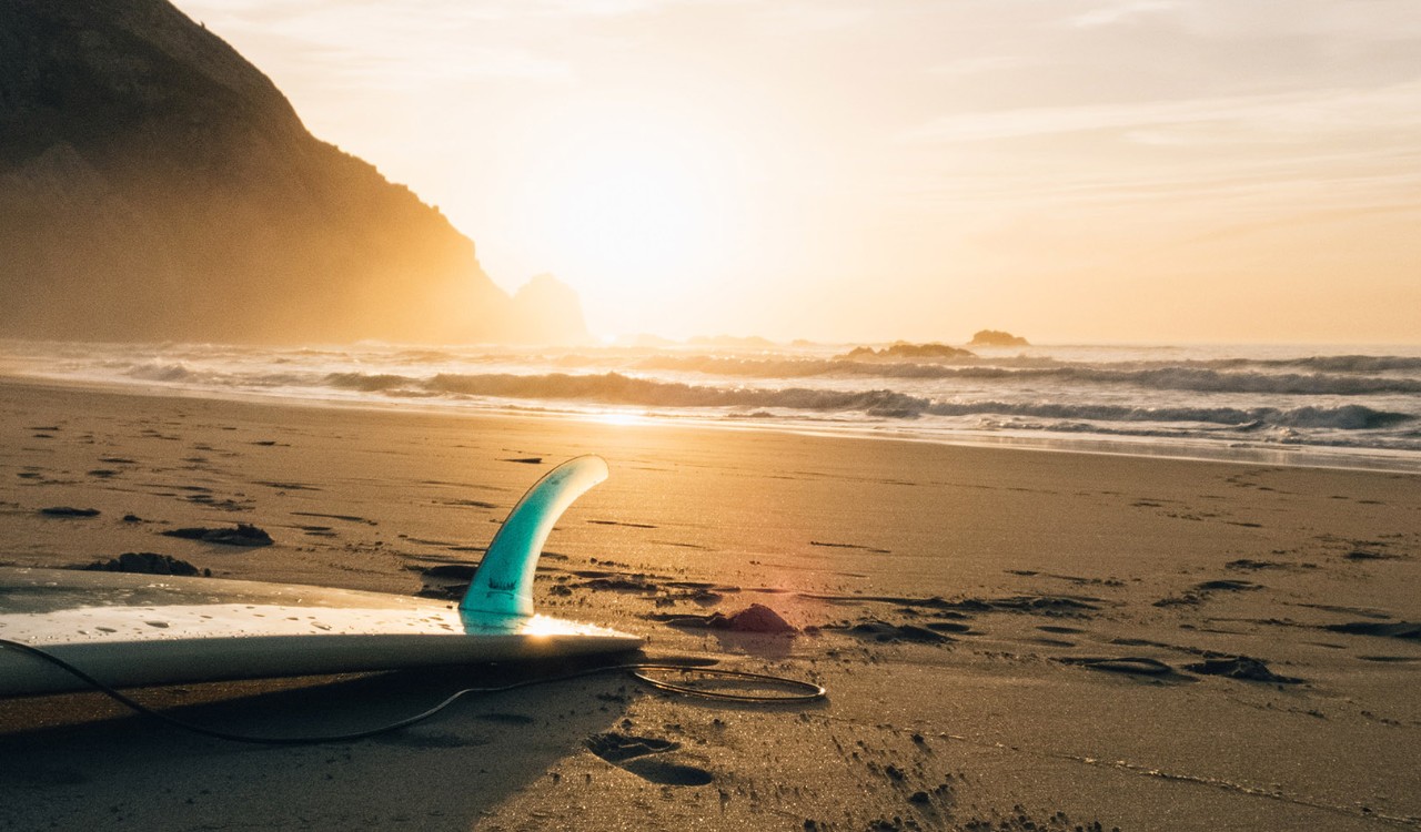 Surfebrett på stranda i solnedgang. Surfboard on the beach at sunset.