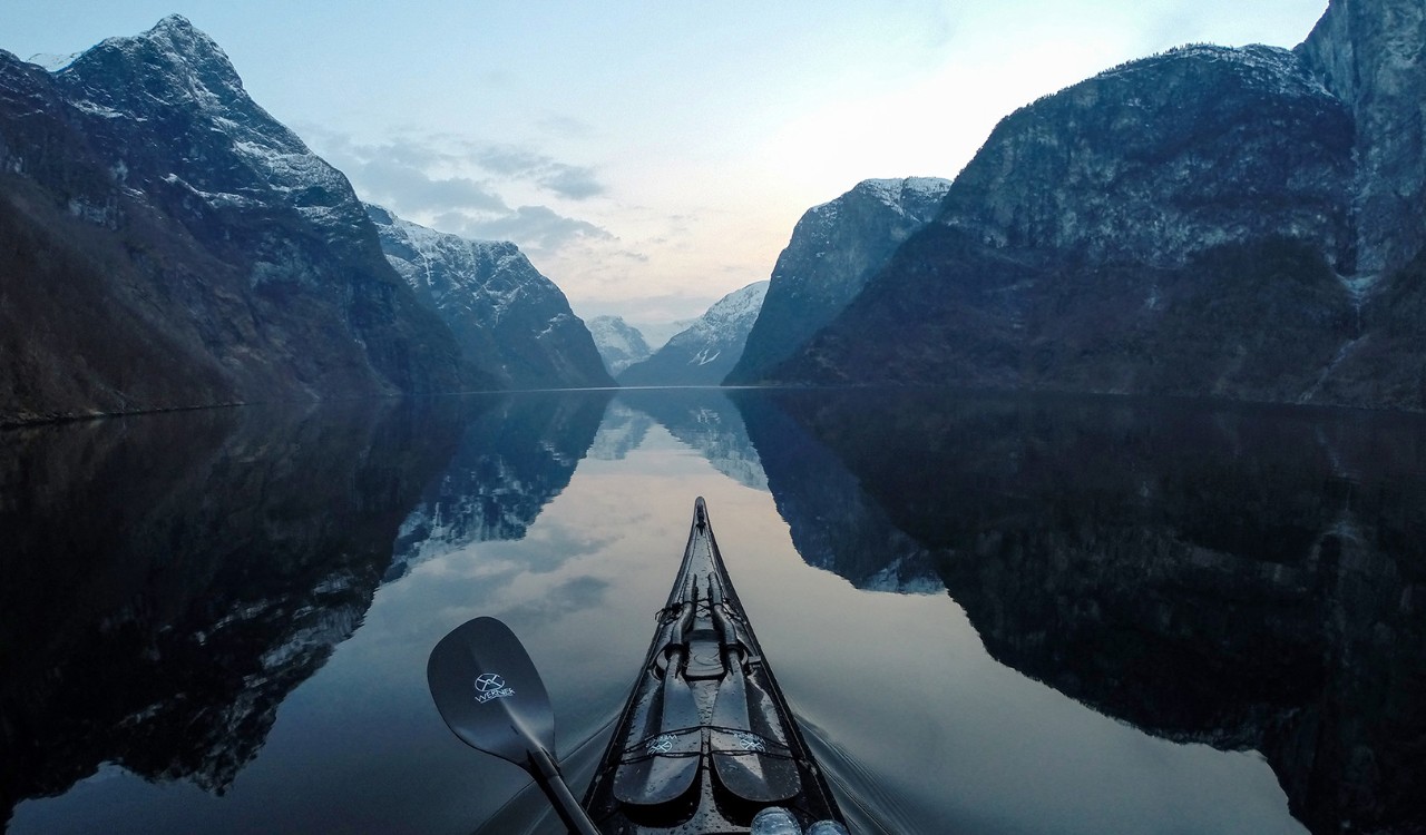 Kajakk glir fram på Sognefjorden med fjell og speilblank fjord. Kayak gliding on at calm fjord with mountains with snow in Sognefjorden. 